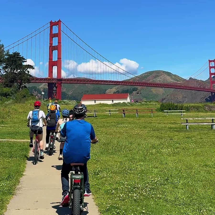 Blazing Saddles riders approaching the Golden Gate Bridge beside a green meadow